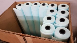 A cardboard box containing several rolls of light blue paper, each with a black core, arranged upright and closely packed together—ideal for flexo printing applications.